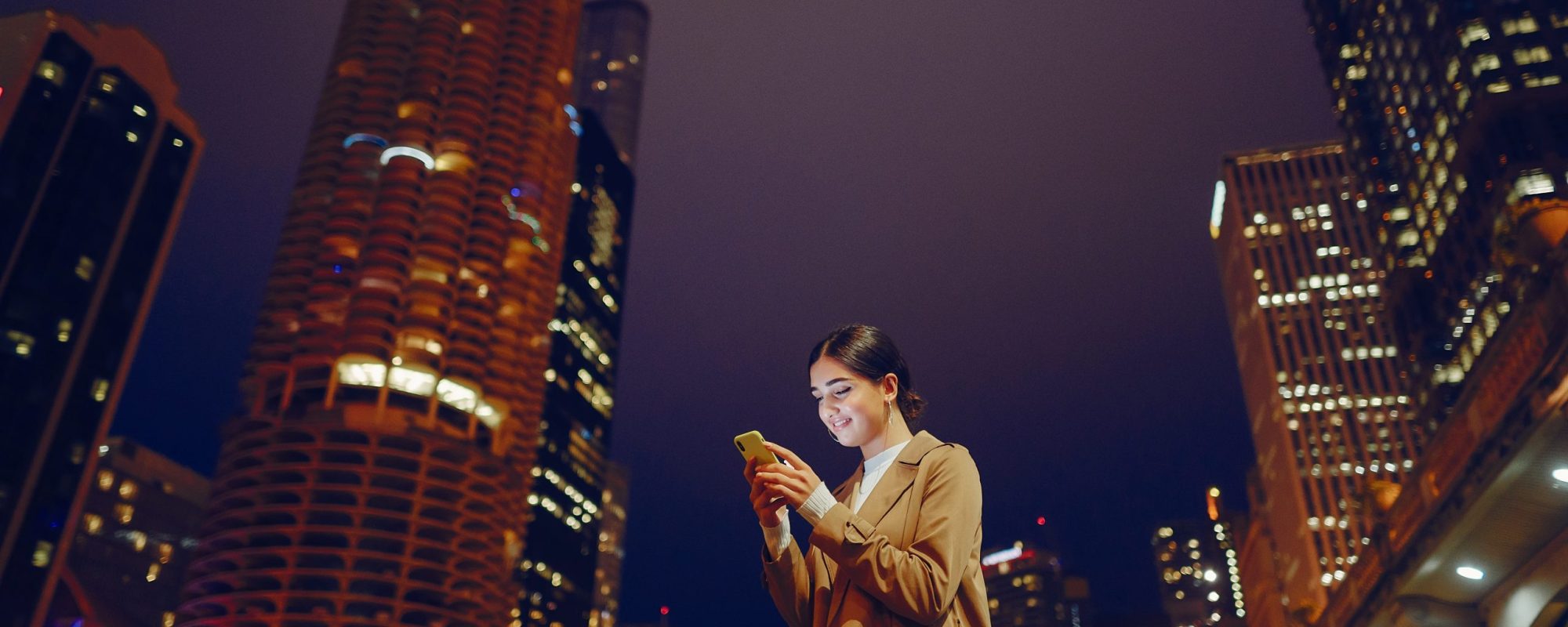 young brunette girl standing at night with phone by Chicago skyline