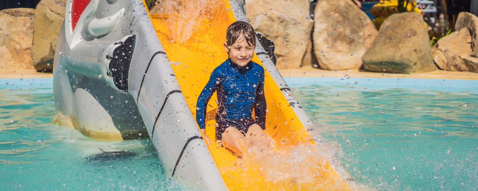 Smiling Young boy riding down a yellow water slide.